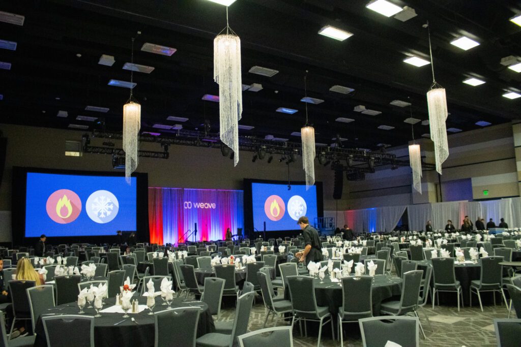 two large projection screens and dining tables for several hundred people